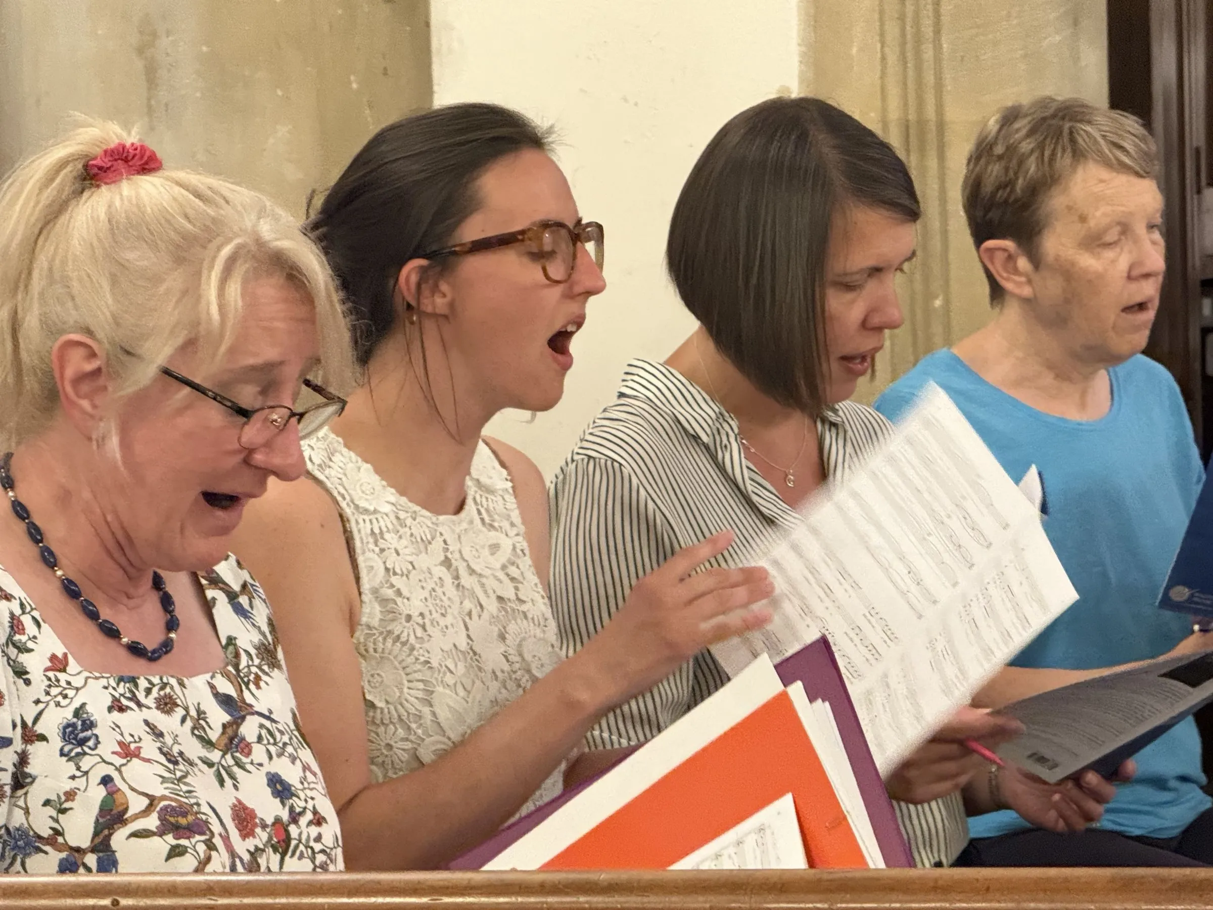 Four singers mid-phrase, scores in hand, one of them laughing
