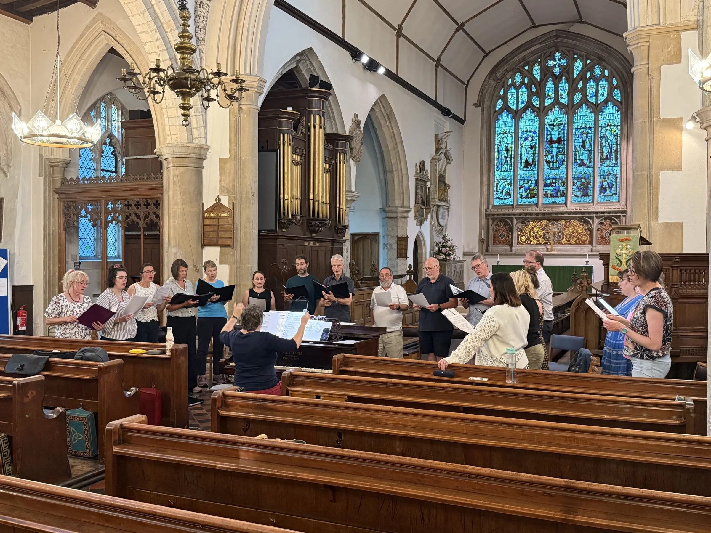 The full choir standing in a horseshoe around the piano, singing from scores