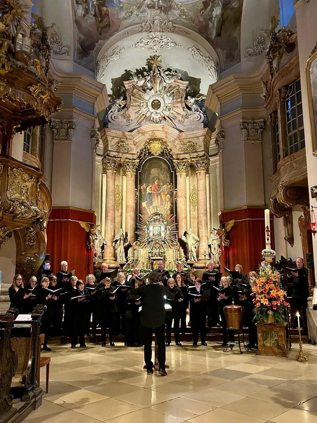 The choir singing before the gilded high altar of a Baroque church