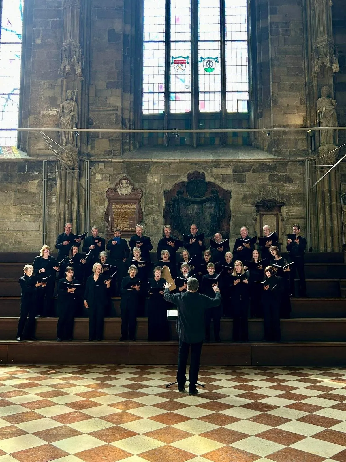 The choir in concert black on raised steps in a Gothic church, the conductor in front, stained glass above